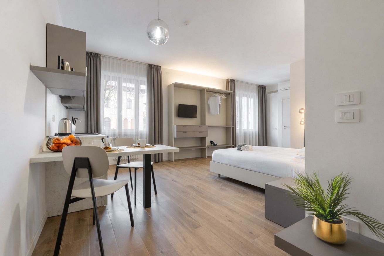 A modern hotel room with a bed, a desk with a chair, a television, and a potted plant.