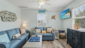 Ein Wohnzimmer mit zwei Sofas, einem Couchtisch, einem Fernseher, Wanddekoration und einem Deckenventilator.
