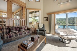 A spacious living room with a plaid sofa, a grey armchair, a round cushioned chair, and a wooden coffee table. - 5-STAR Lakefront cabin with AMAZING mountain & lake VIEWS! DOCK & GAME ROOM! (Big Bear Lake)
