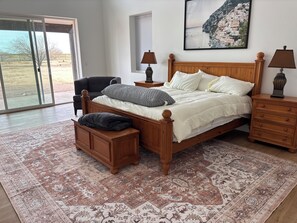 A bedroom with a wooden bed, a nightstand, a chair, a window with blinds, and a rug. - Enjoyable family friendly 4-bedroom Solar home close to Atessa Podium Club, (Casa Grande)