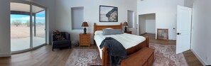 Quarto com cama, cadeira, mesa de cabeceira, luminária, moldura de quadro e vista através de uma porta de vidro deslizante.