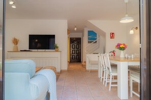 Ein modernes Wohnzimmer mit Sofa, Fernseher und Essbereich mit Stühlen und Tisch.
