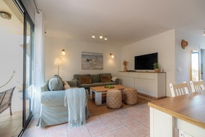 Ein Wohnzimmer mit einer Couch, einem Couchtisch, Hocker, einem Fernseher und einem Essbereich.