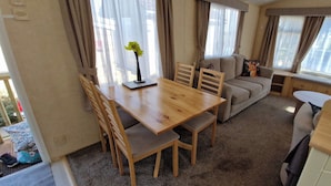 A cozy living area with a wooden dining table, cushioned chairs, a sofa, and a window with curtains. - Fieldview Lodge Dog Friendly nr Anderby Creek (Alford)