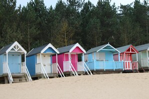 Fileira de cabanas de praia com escadas que levam à entrada, com um cenário de árvores ao fundo.