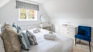 Un dormitorio con cama, almohadas, mesita de noche, cómoda, silla, ventana con vistas y un reloj de pared.