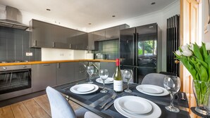 Una cocina moderna con armarios oscuros, horno integrado y una zona de comedor con mesa de vidrio para dos.