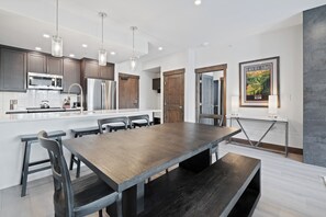 A modern kitchen with stainless steel appliances, a wooden dining table, and pendant lighting. - Beaver Creek Slope-Side Luxury | UB306 (Beaver Creek)