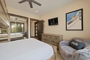 Ein Schlafzimmer mit Bett, Kommode, Fernseher, einer Couch und einer Schiebetür zum Balkon.