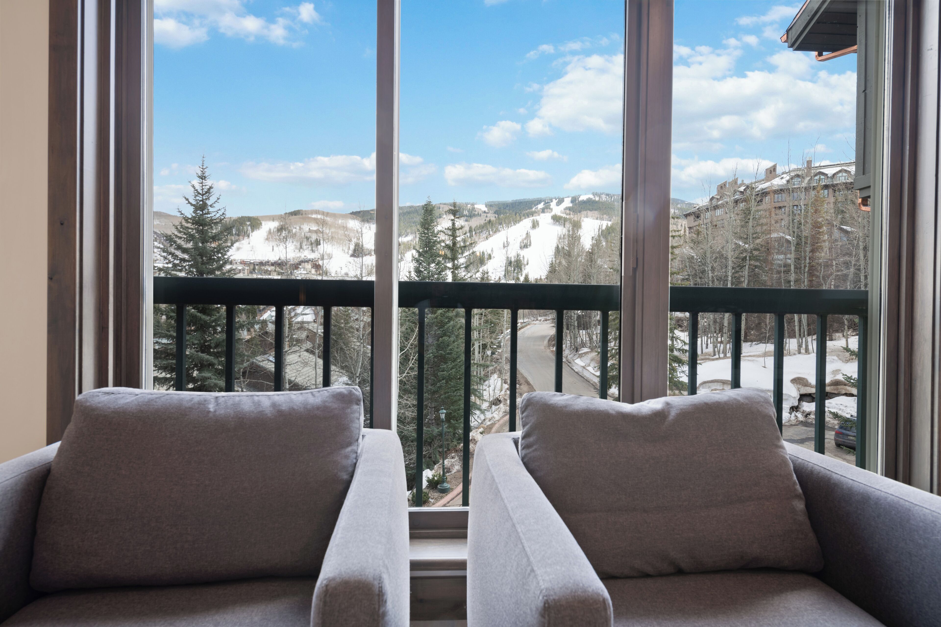Una habitación con un ventanal grande, dos sofás grises y vistas a un paisaje montañoso nevado.
