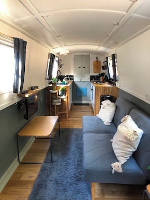 A compact RV interior with a kitchenette, a sofa, and a small table.