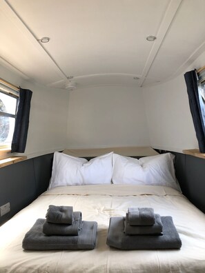 A bed with white pillows and a beige bedspread, two folded towels, and a window with curtains.