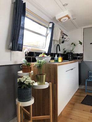 A compact kitchen with a window, a sink, a small island with a plant, and a stool.