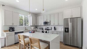 Una cucina moderna con mobili bianchi, elettrodomestici in acciaio inossidabile, un'isola centrale con sgabelli da bar e illuminazione a sospensione.