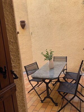 A patio with a table and chairs, a potted plant, and a textured wall.