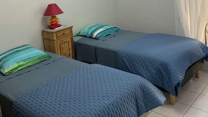 Een kamer met twee bedden, een nachtkastje, een lamp en een plafondarmatuur.