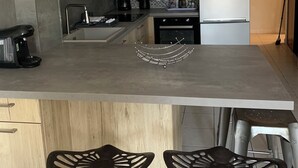 Een moderne keuken met een magnetron, koffiezetapparaat en een koelkast. Er staan twee barkrukken bij de spoelbak.