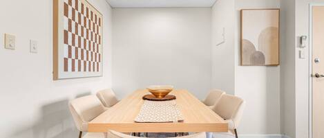 A dining area with a wooden table, beige chairs, a ceiling fan, and artwork on the walls.