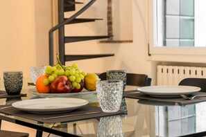 Ein Esstisch mit Obstschale, Gläsern und Tellern, in einem modernen Raum mit Treppe und Fenster.