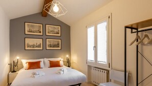 Ein Schlafzimmer mit Bett, Nachttischlampen, Heizkörper, Fenster und Kleiderständer.