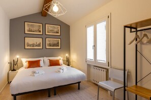 Ein Schlafzimmer mit Bett, Nachttischlampen, Heizkörper, Fenster und Kleiderständer.