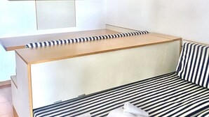A room with a sofa and a bed with striped bedding, a wooden bench, and a wall-mounted shelf. - Porto Rotondo Bilo4 A208 in residence with swimming pool (Porto Rotondo)