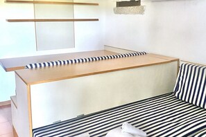 Ein Zimmer mit einer Couch und einem Bett mit gestreifter Bettwäsche, einer Holzbank und einem an der Wand befestigten Regal.