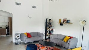 Un salon moderne avec deux canapés gris, un fauteuil en forme de poire bleu, une chaise jaune, une table basse noire et une bibliothèque.
