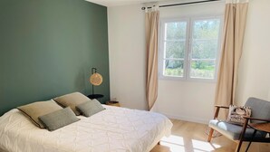 Une chambre à coucher avec un lit, une chaise, une table de chevet, une lampe et une fenêtre avec des rideaux.