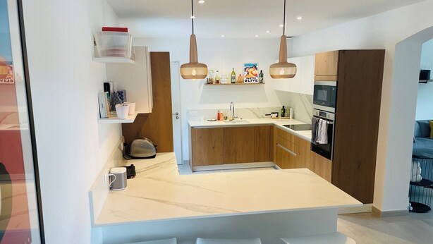Une cuisine moderne dotée d’un îlot central, de meubles en bois, d’un four encastré et d’un luminaire suspendu.