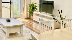 Een woonkamer met een televisie, witte meubels, een plant en een schuifpui.