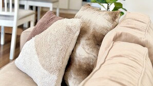 Een woonkamer met een beige bank, een potplant en een eethoek op de achtergrond.