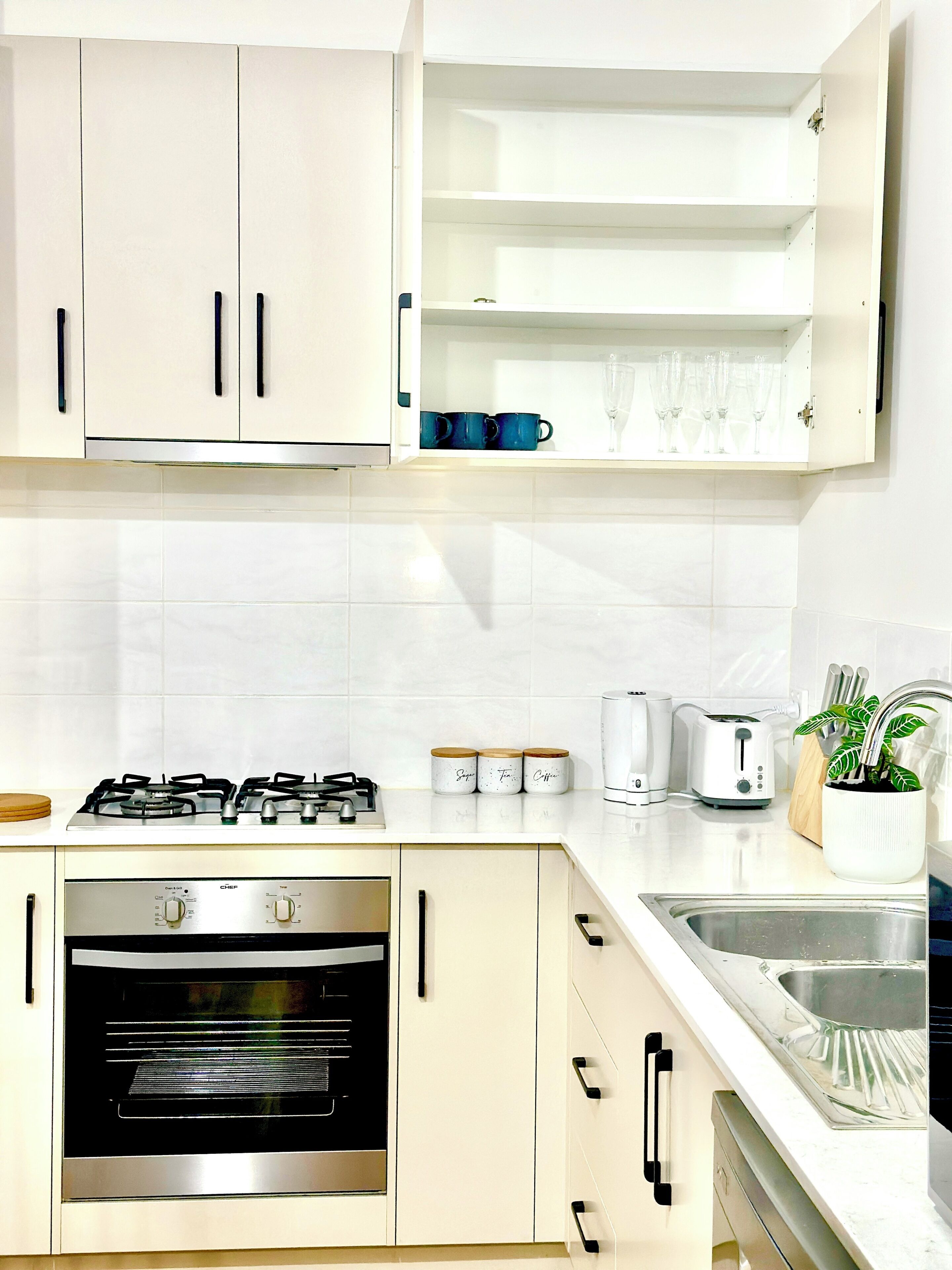 A modern kitchen with white cabinets, a gas stove, an oven, a toaster, and a sink.