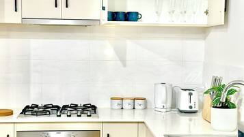 A modern kitchen with white cabinets, a gas stove, an oven, a toaster, and a sink.