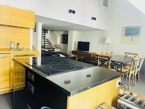 A modern kitchen with a central island, a dining area with wooden chairs, a TV, and a staircase leading to another level. - Large apartment in the center of CAUTERETS (Cauterets)