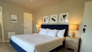 Un dormitorio con cama, dos mesitas de noche, cabecero y decoración en la pared.