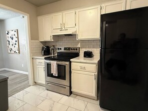 Eine Küche mit weißen Schränken, einem schwarzen Kühlschrank und einem Edelstahlbackofen.