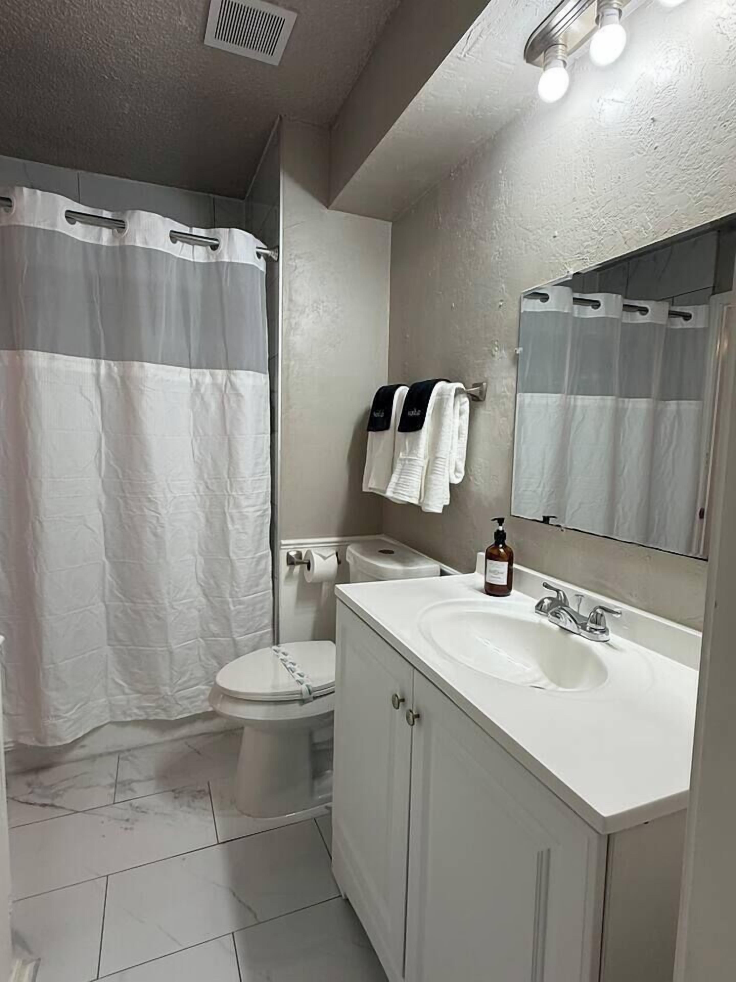 A bathroom with a shower curtain, toilet, sink, mirror, and towel rack.