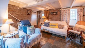 Ein gemütliches Zimmer mit einer Steinwand, einem Sofa, einem Sessel, einem kleinen Tisch und einer Lampe.