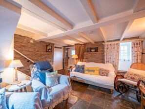 Une pièce chaleureuse avec un mur en pierre, un canapé, un fauteuil, une petite table et une lampe.