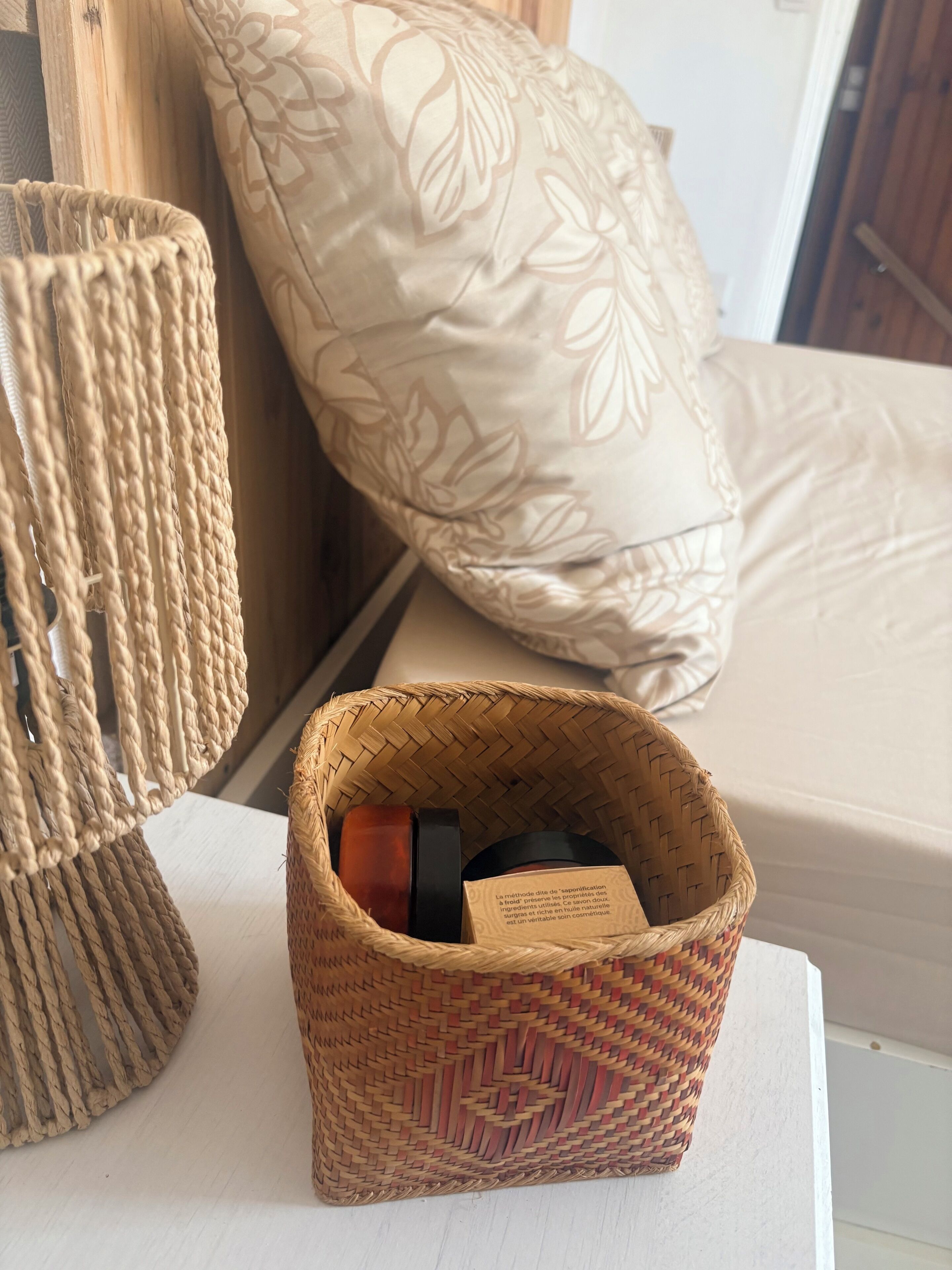 A wicker basket with a label on a white surface, a woven chair, and a patterned pillow.
