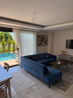Ein Wohnzimmer mit einer Couch, einem Fernseher, Blick auf einen Pool und einem Gemälde an der Wand.