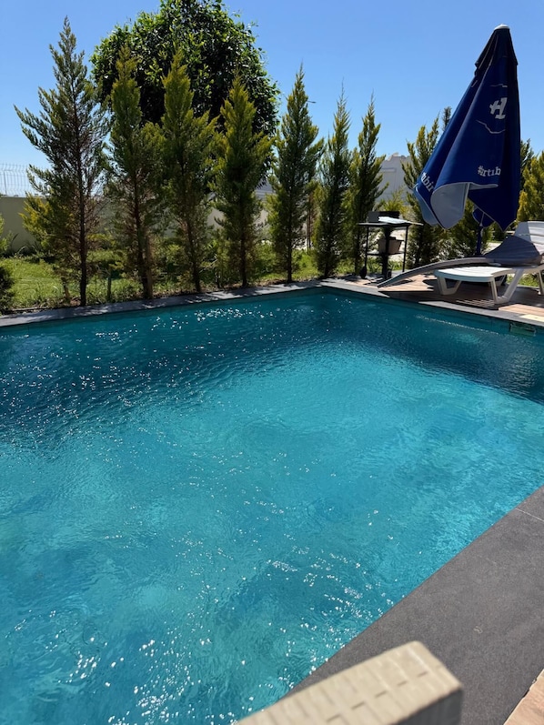 A clear swimming pool with a blue umbrella and lounge chairs.