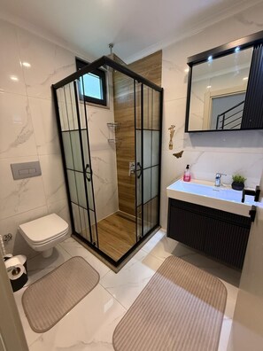Ein modernes Badezimmer mit Duschkabine, Toilette, Waschbecken mit Spiegel und Handtuchheizkörper.