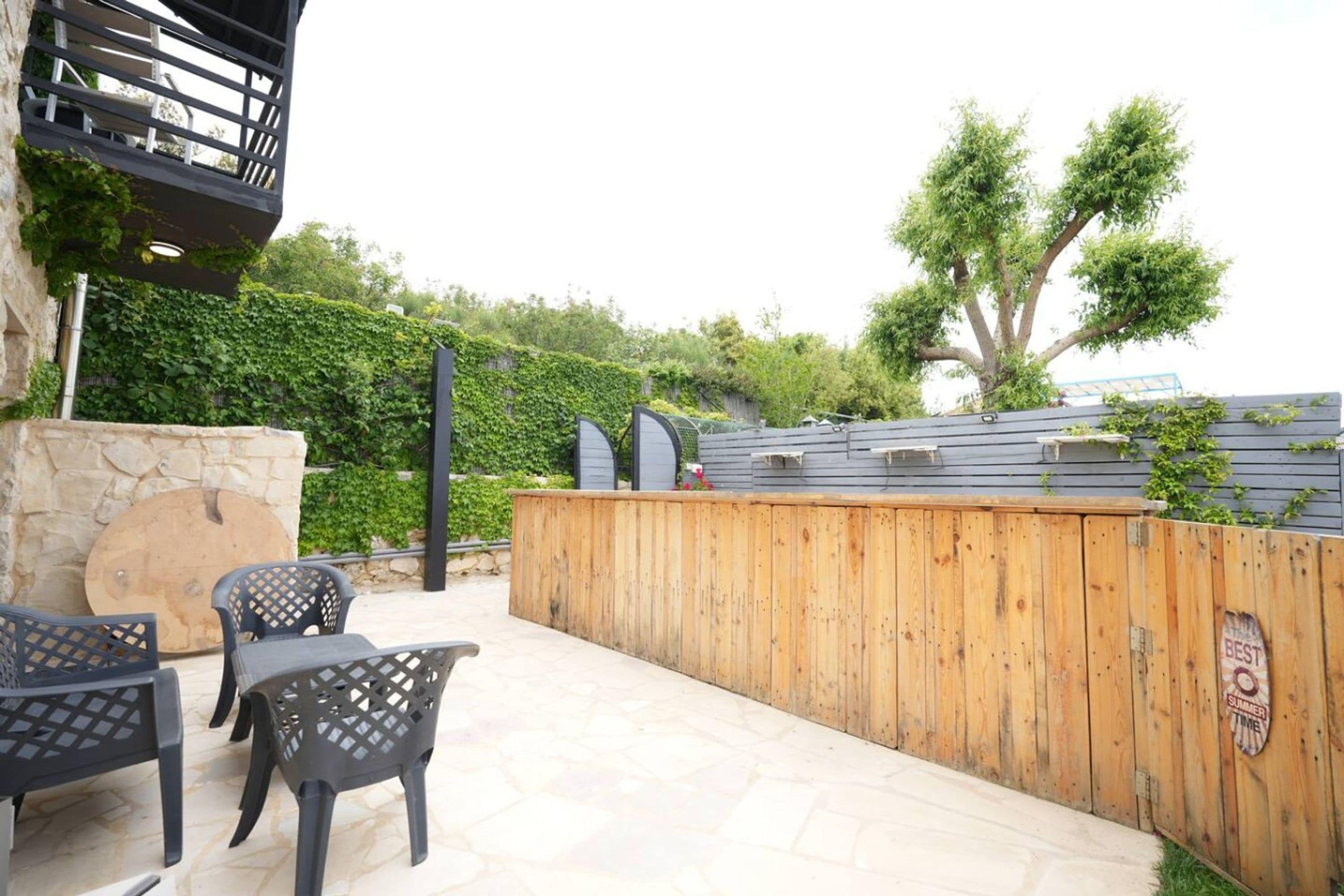 An outdoor patio with stone flooring, wooden fence, and black chairs.