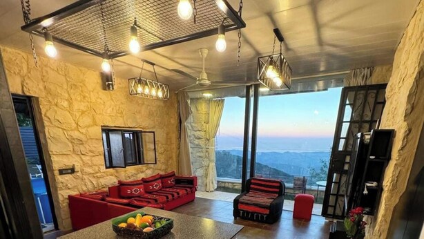Un intérieur moderne avec un îlot de cuisine, des tabourets de bar, un canapé rouge et une vue sur les montagnes.