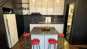 Une cuisine compacte dotée d’un îlot central, de quatre tabourets de bar et d’un réfrigérateur.