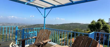 A covered outdoor seating area with blue railings, wooden chairs, and a view of the landscape.