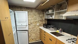 A compact kitchen with a refrigerator, stove, sink, and wooden cabinets. - Alali s Guesthouse With tub (Aalali)