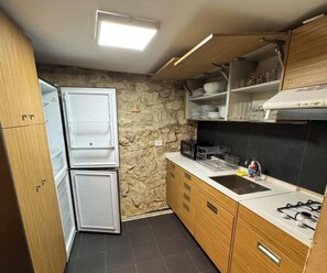 A compact kitchen with a refrigerator, stove, sink, and wooden cabinets. - Alali s Guesthouse With tub (Aalali)